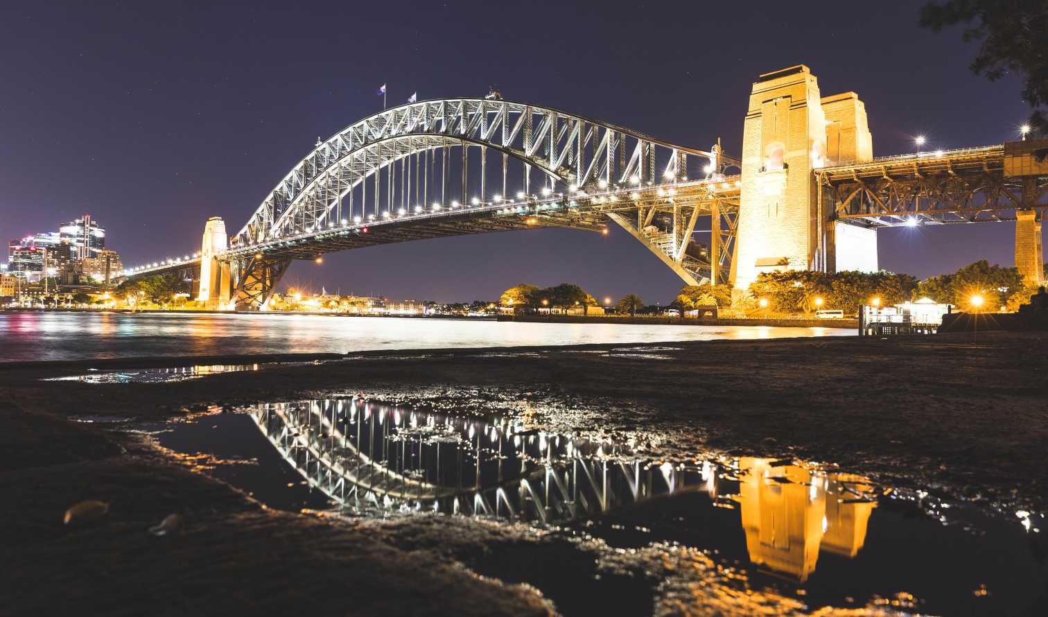 Sydney Harbour Bridge at night with lights reflecting in water.