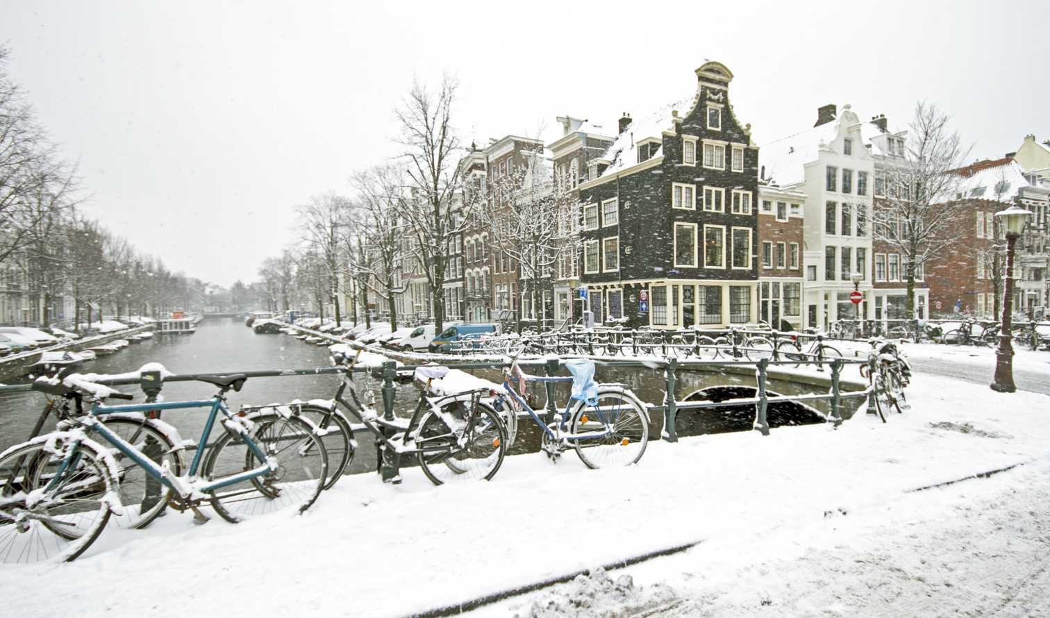 Snow-covered bicycles on a bridge over an Amsterdam canal.