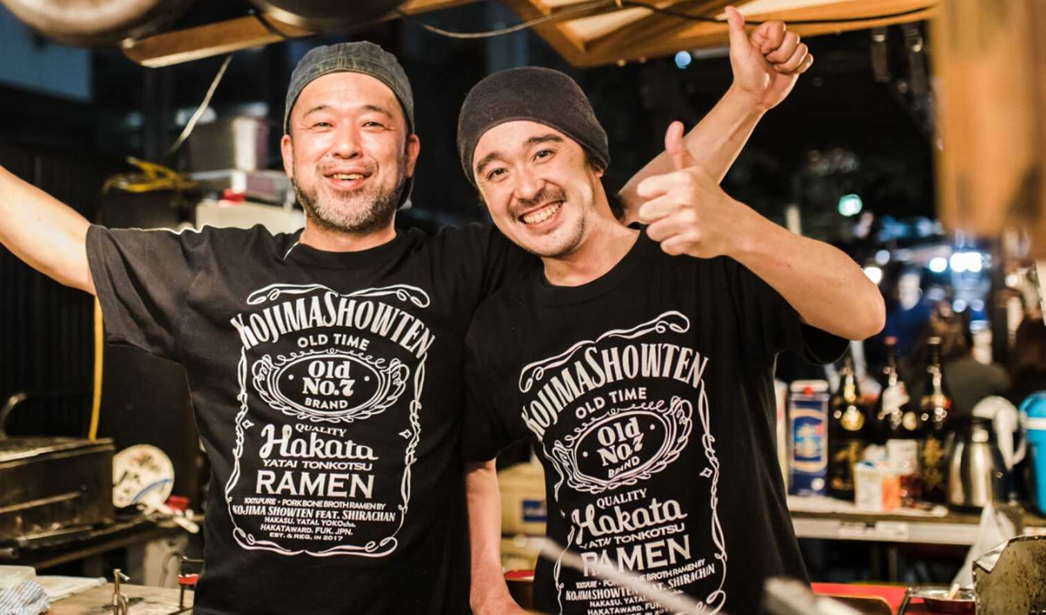 Two men in black shirts at a street food stall in Fukuoka.
