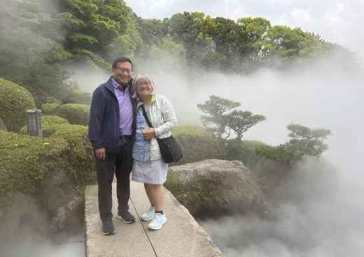 Two people standing on a walkway in a foggy Japanese garden.