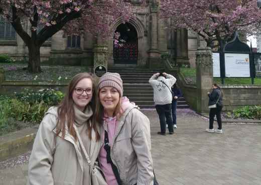 Two people standing in front of Manchester Cathedral with cherry blossoms.