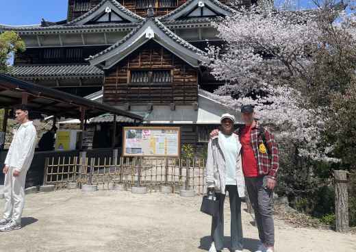People stand in front of Hiroshima Castle with cherry blossom trees in the background.
