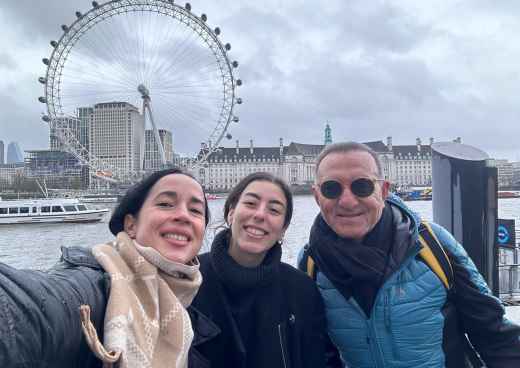 Visitors standing near the River Thames with the London Eye behind.