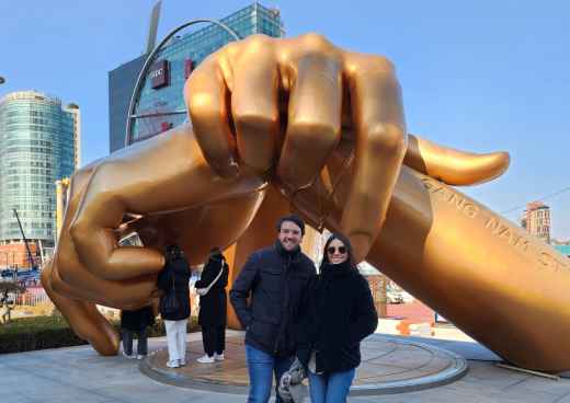 Two people stand in front of the Golden Hand sculpture in Gangnam, Seoul.