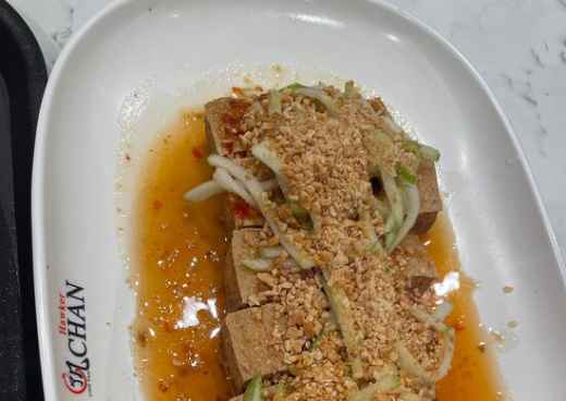 Plate of tofu topped with chopped nuts and sliced vegetables at Hawker Chan.