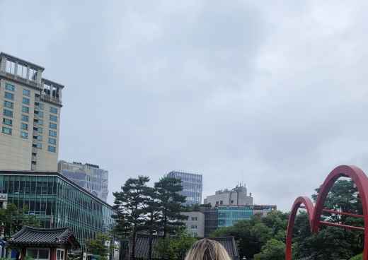 Back view of a person surrounded by lush greenery and urban architecture.