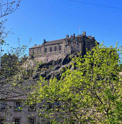 View of Edinburgh Castle from a lower perspective with green trees in the foreground.