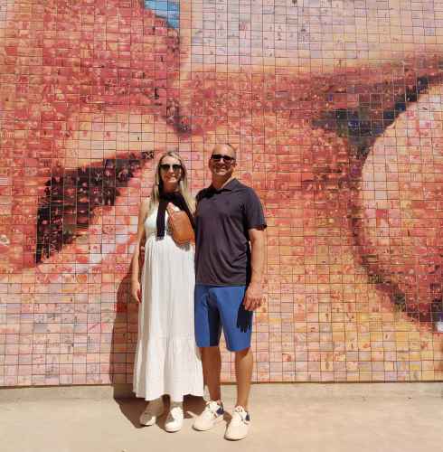 Two people stand in front of the 'El Beso' mural in Barcelona.