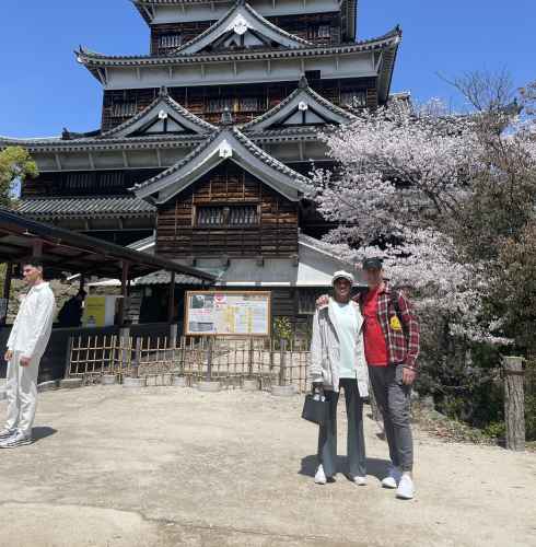 People stand in front of Hiroshima Castle with cherry blossom trees in the background.