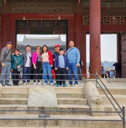 Family standing in front of traditional gate at Gyeongbokgung Palace.