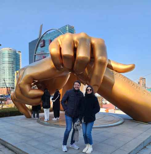 Two people stand in front of the Golden Hand sculpture in Gangnam, Seoul.