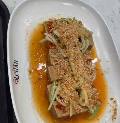 Plate of tofu topped with chopped nuts and sliced vegetables at Hawker Chan.