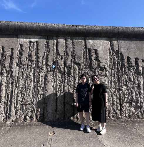Two people standing in front of the Berlin Wall remains.