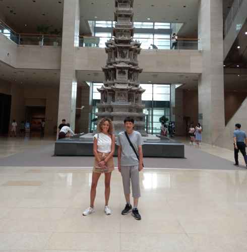 People standing in front of a tall stone pagoda inside a spacious museum hall.