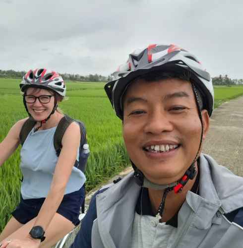 Man and woman cycling on a path with green fields surrounding them.