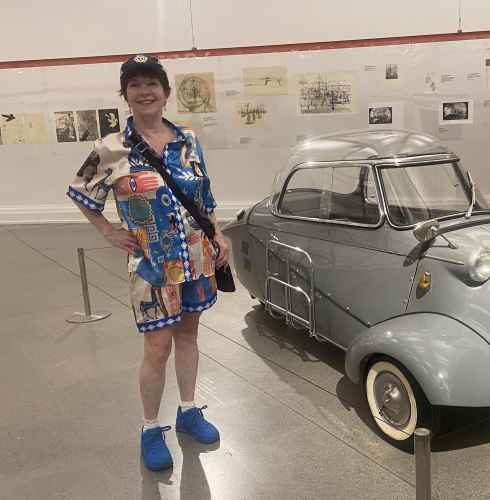 Woman in colorful attire beside a microcar display indoors.