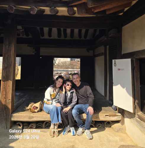 Three people sitting on a wooden platform in a traditional Korean house.