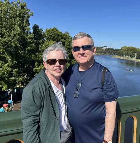 Two people standing on a bridge over ta river in Melbourne.