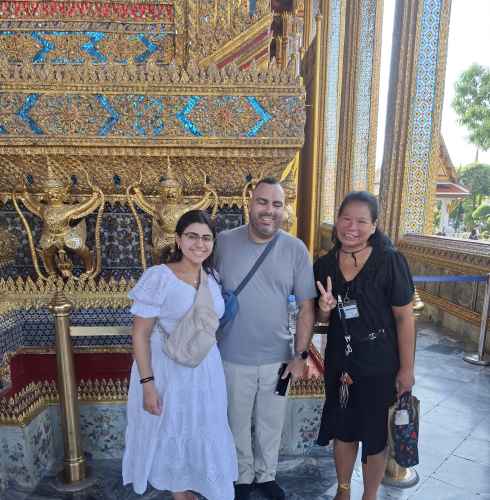Three people standing in front of ornate architecture at the Grand Palace, Bangkok.