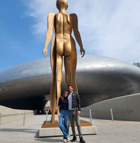 Two people stand in front of a large golden sculpture at Dongdaemun Design Plaza.