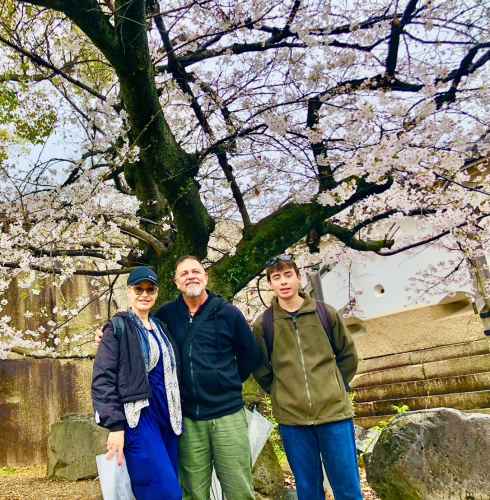 Tourists standing under cherry blossoms in full bloom, smiles all around.