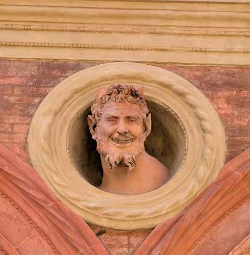 A mischievous stone face peers from Bologna's intricate brickwork.
