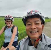 Man and woman cycling on a path with green fields surrounding them.