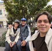 Three people sitting on a bench in a plaza with colonial architecture
