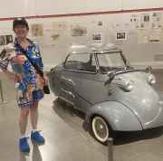 Woman in colorful attire beside a microcar display indoors.