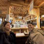 Two women seated at a sushi counter with a chef preparing food in Tokyo.