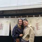 Two people standing in front of a restaurant with Japanese signage.