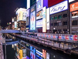 Reflected neon signs at dusk along the Dotonbori canal with crowds visible on the walkway. Reflected neon signs at dusk along the Dotonbori canal with crowds visible on the walkway.