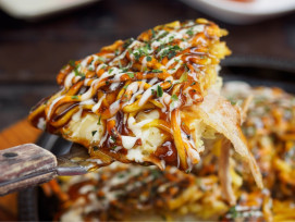 A close-up of sizzling okonomiyaki on a teppan grill, surrounded by small bowls of sauces and condiments, with a local chef mid-flip and steam rising under warm lighting A close-up of sizzling okonomiyaki on a teppan grill, surrounded by small bowls of sauces and condiments, with a local chef mid-flip and steam rising under warm lighting