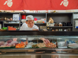 A guide talking with guests about seasonal foods at a fresh market stall.