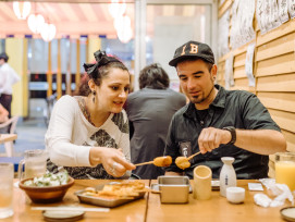 Grilled kushikatsu being served in a small restaurant as a guide talks with guests. Grilled kushikatsu being served in a small restaurant as a guide talks with guests.