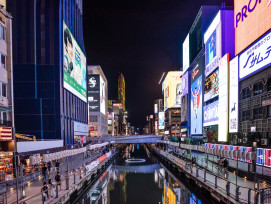 Vibrant neon signs reflecting in Dotonbori canal waters during evening hours with crowds below