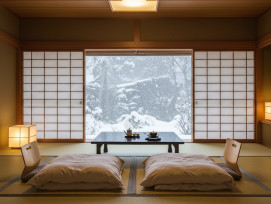 A traditional ryokan room with tatami mats and futon bedding, snow visible through paper screen windows A traditional ryokan room with tatami mats and futon bedding, snow visible through paper screen windows