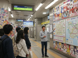 Local host explaining train system with anime advertisements visible.
