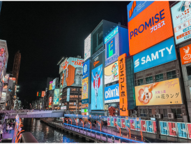 Bustling evening street scene in Dotonbori with neon signs and food vendors.