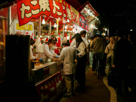 Multiple takoyaki vendors lined up along Dotonbori street with bright signage. Photo by HANVIN CHEONG on Unsplash