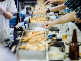 Traditional kushikatsu restaurant with customers standing at outdoor counters.