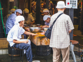 Elder vendor teaching younger family member traditional street food preparation techniques. Photo by Luca Dal Molin on Unsplash