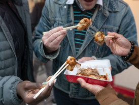 Locals enjoying hot takoyaki from a street vendor on a chilly December evening