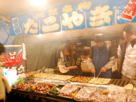 Colorful Osaka street food market with smoke rising from takoyaki stalls. Image by chou_i_ci from Wiki Commons