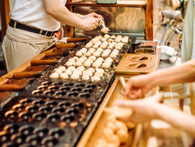 Takoyaki being flipped at street food stall.