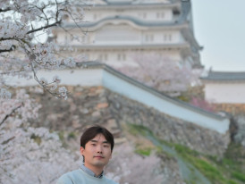 Solo traveler standing thoughtfully before the impressive stone walls of Osaka Castle, with cherry blossoms framing the scene. Image by Gavin Li on Unsplash.