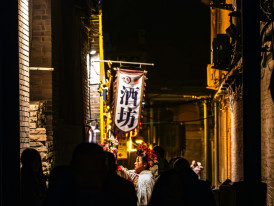 A friendly local host gesturing animatedly while walking with guests through the narrow, lantern-lit streets of Ura Namba. Image by Kilian Murphy on Unsplash.