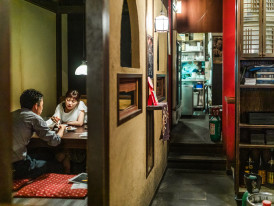 A cozy, traditional izakaya tucked into a narrow alley, with warm light spilling from its entrance and traditional lanterns creating an intimate atmosphere.