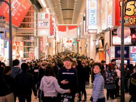 A local host guiding guests under the bright neon signs of a busy entertainment district, with everyone smiling and engaged in animated conversation. Image by Satoshi Hirayama on Pexels.