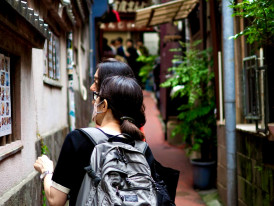 A confident solo traveler walking alongside a friendly local host through a traditional neighborhood, both engaged in animated conversation. Image by Kazuo Ota on Unsplash.